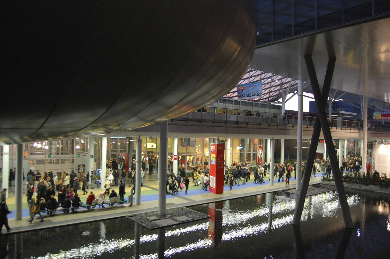 Corso centrale coperto del quartiere fieristico di Fiera Milano Rho con i visitatori lungo lo specchio d’acqua